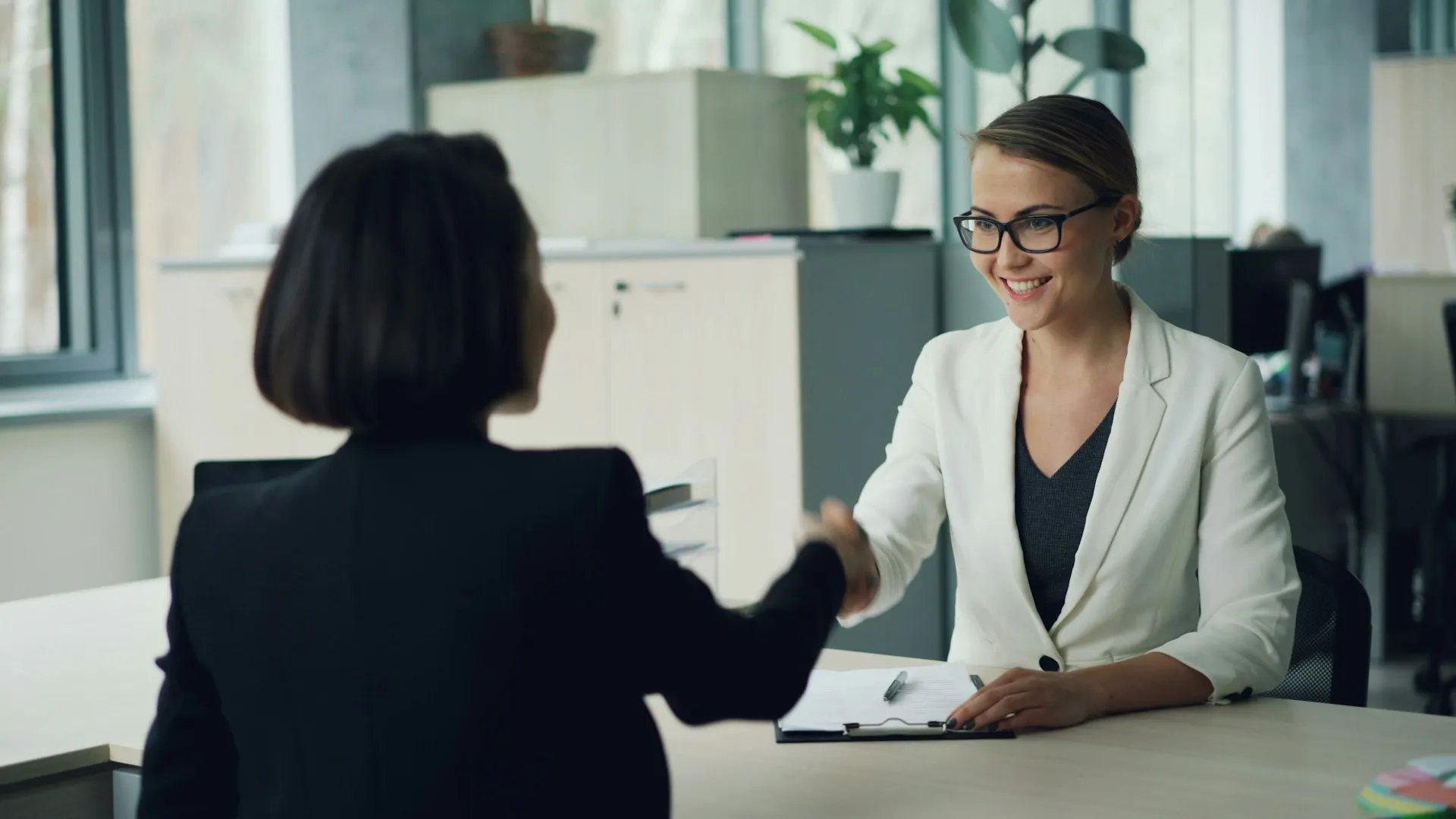Zwei Frauen geben sich am Schreibtisch die Hand